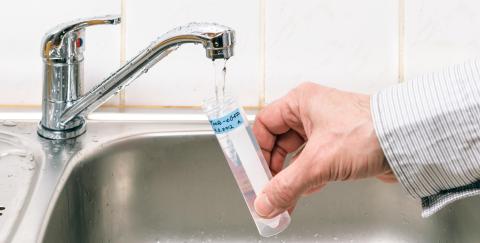 Hand holding a test tube under a running faucet for water analysis