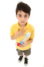 A child holding inhaler and a spacer chamber in one hand and other hand to his chest.