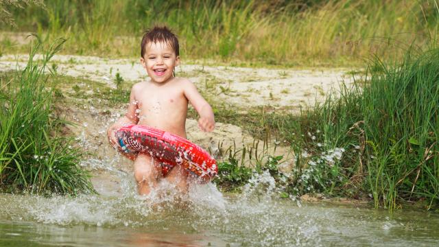 A happy young child with inner tube run to lake.