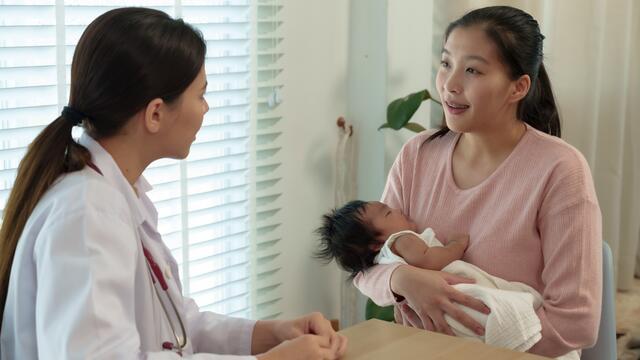 Mom holding a newborn talks with a doctor in their office