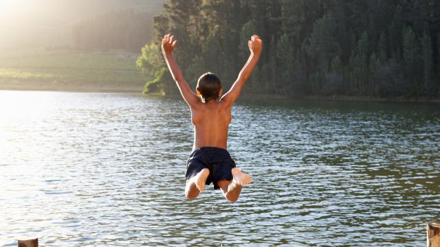 Young child jumping into lake from a pier with arms up