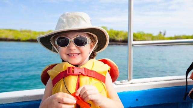 Young child wears a life vest, sun hat and glasses on a boat