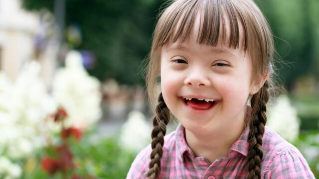A portrait of a smiling child with down syndrome outside