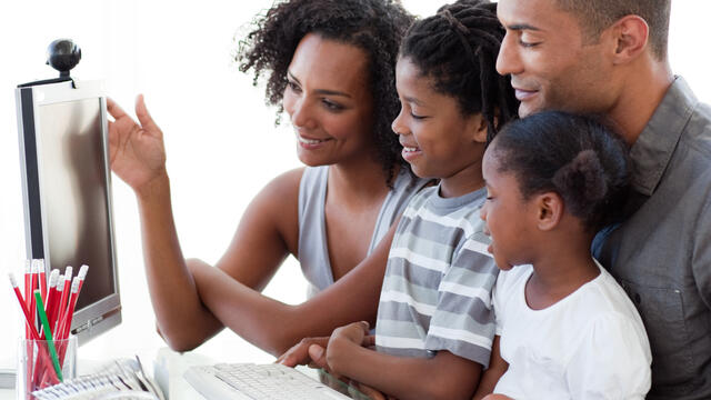 Two adults and two children gathered around a home computer.