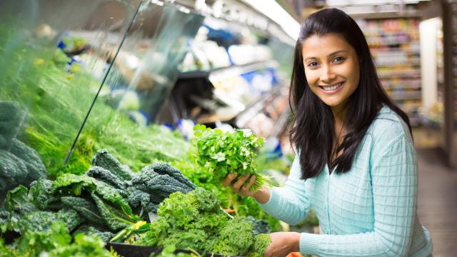 A person chooses cilantro among leafy greens at a grocery store