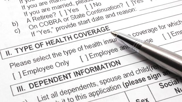 Close-up of an insurance form, type of health coverage and dependent information, with a pen resting on the paper