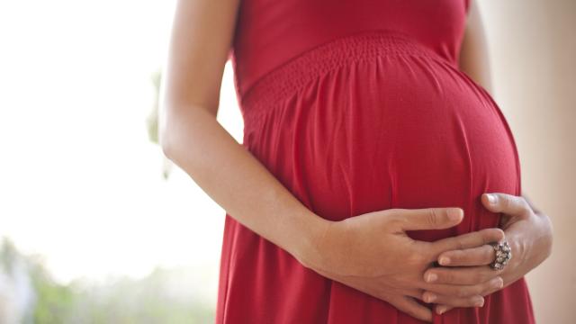 Clasped hands lay across her pregnant belly in red dress