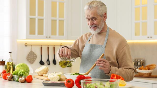 Older adult pouring oil over a salad in a kitchen