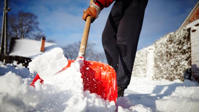 A person cleans the sidewalk with a snow shovel