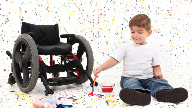 Child on the floor splatters paint a white room with a wheelchair close by