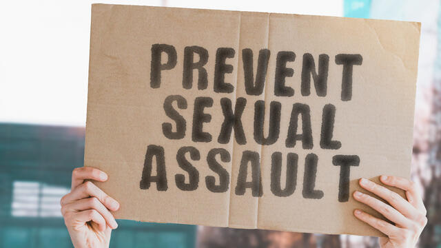 Adult hands hold a Prevent Sexual Assault sign on cardboard