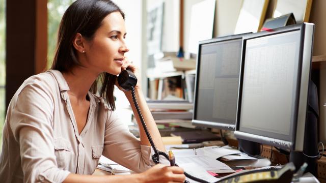 Person sitting at desk, looking at computer while on phone