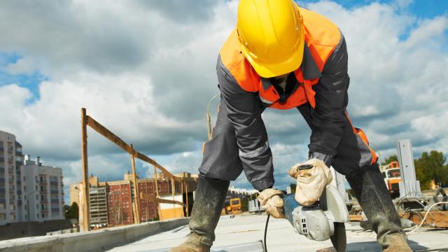 Construction worker with hard hat, uses a grinder on a site