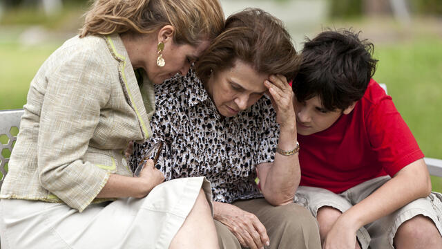 Upset adult receiving support from another adult and a teen outside.