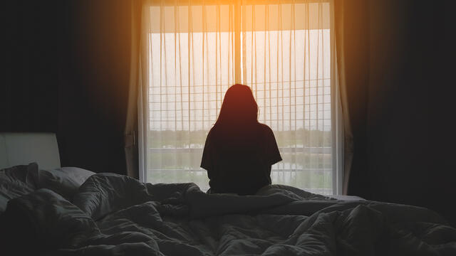 Silhouette of a person sitting bedside looking out a sunlight window