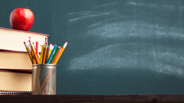 Desk with a stack of books, pencil cut and apple in front of a blackboard