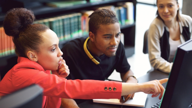 Three young adults working together on a computer.