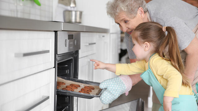 Toddler with grandmother, taking cookies out of the oven