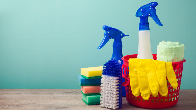 A red bucket with cleaning supplies, sponges and gloves.