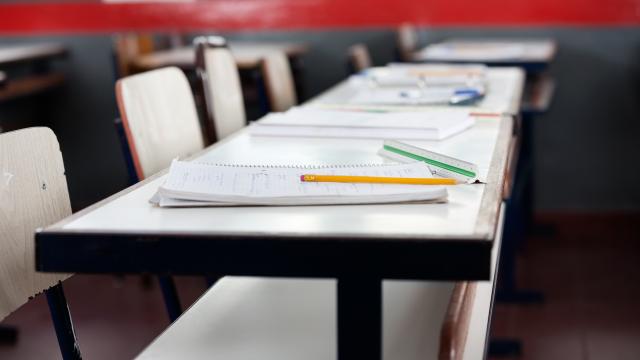 Empty classroom, a desk and notebooks with a red bar across on the top