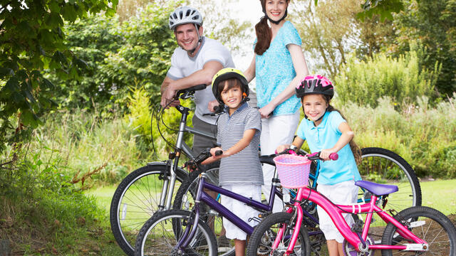 A smiling family of four with their bicycles in a park.