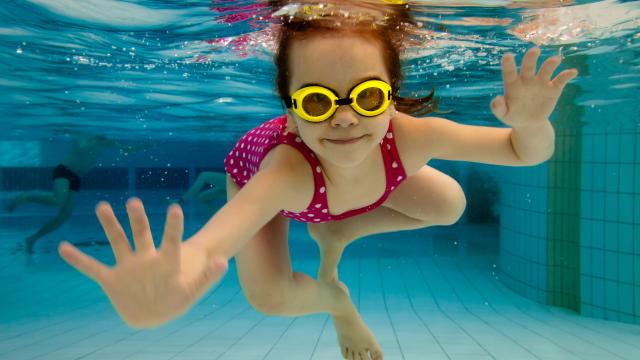 A happy child swims under water in a pool.