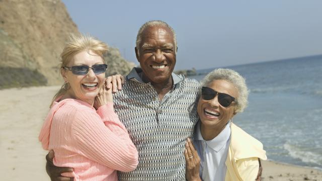 Three smiling adults hugged by a beach.