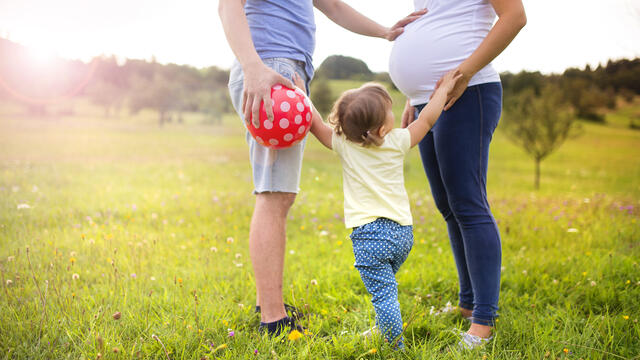 Two adults holding the hands of a child while one has their hand on the other's pregnant belly