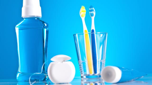 Mouthwash, dental floss, toothpaste, and toothbrushes in a clear glasses