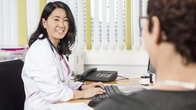 Doctor uses the computer while discussing with a patient in the office