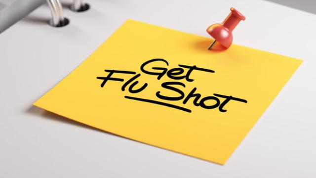 A red pushpin pinned a yellow note with "Get flu shot" written on it to a white notebook