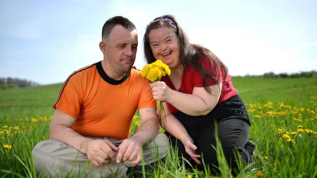 Two adults, one smiling holding yellow dandelions in a field