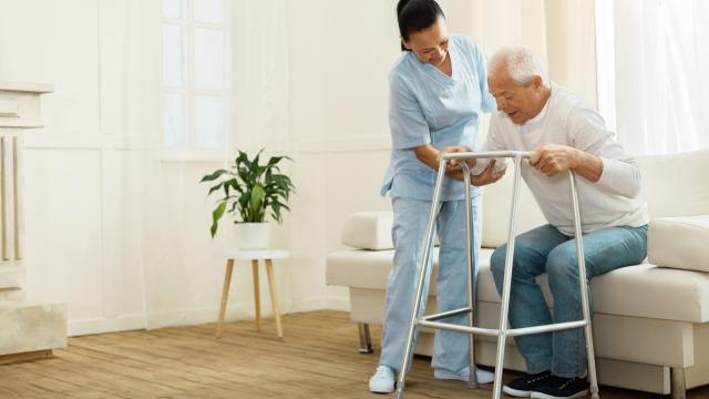 Caregiver assisting an adult with a walker to rise from sofa