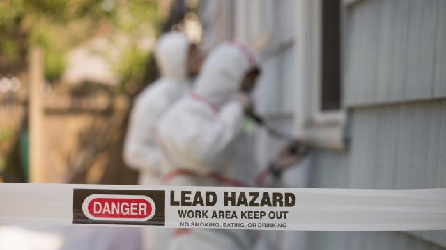 Danger, Lead Hazard tape and adults in hazmat suits removing lead paint outside