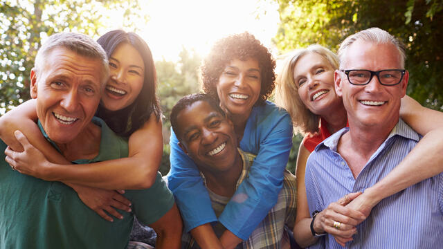 Adults giving piggyback rides to other three adults outside, all laughing.