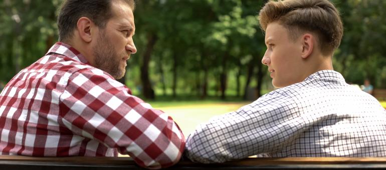 An adult and a teen sitting on a bench talking