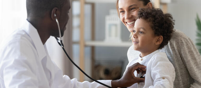 Toddler sitting on adult lap while doctor listens to his heart