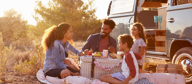 A family of four enjoy picnic next to their van.