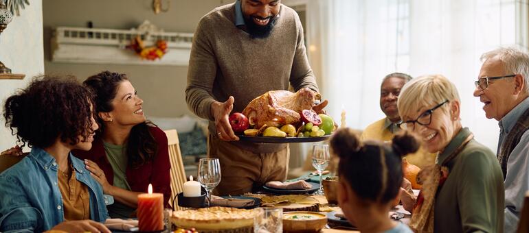 Family gathered at holiday dinner table as adult brings in turkey
