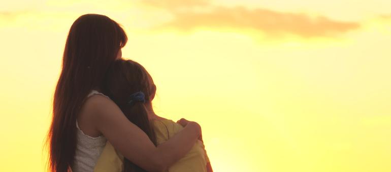 Adult hugging a child at sunset