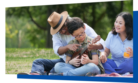 Adult holding glass watching another adult showing a child how to play a ukulele outdoors