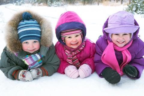 Three children laying on their belly in the snow smiling.