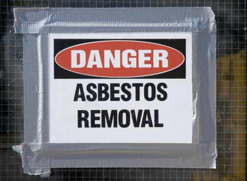 Danger asbestos removal sign taped to a wall with duct tape.