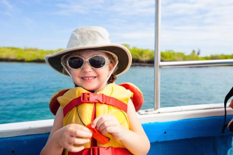 Young child wears a life vest, sun hat and glasses on a boat