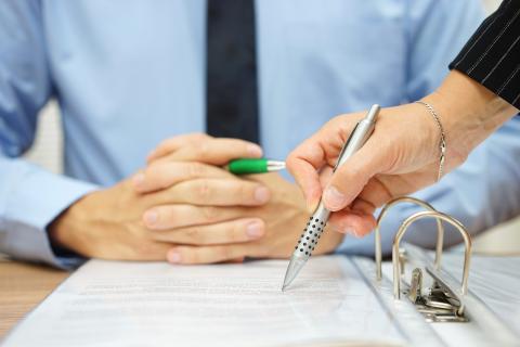 Two people looking at a binder, one writing a note