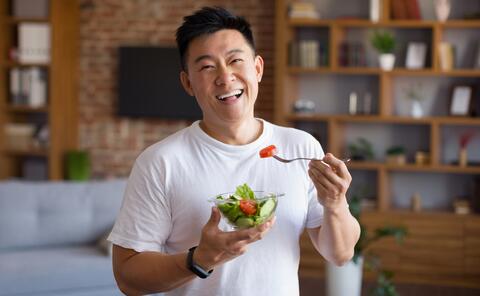 Smiling adult holds a bowl and fork of fresh salad