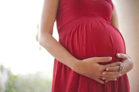 Clasped hands lay across her pregnant belly in red dress