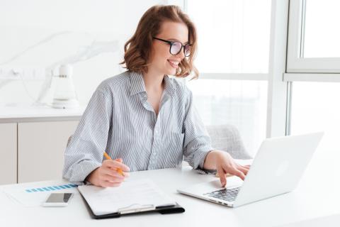 Adult at desk with laptop, clipboard and smart phone
