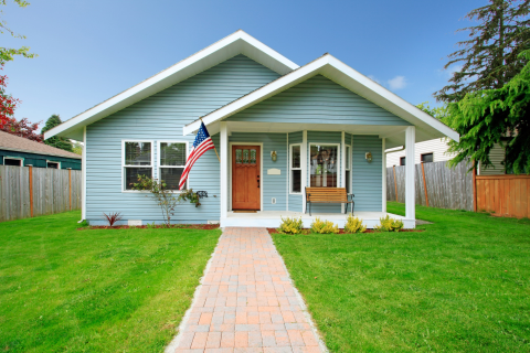 A blue home flying the American flag in the front porch with wooden fence