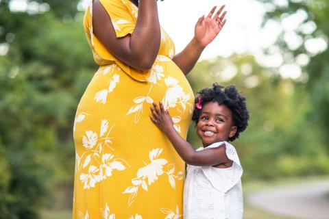 Smiling child hugging a pregnant belly